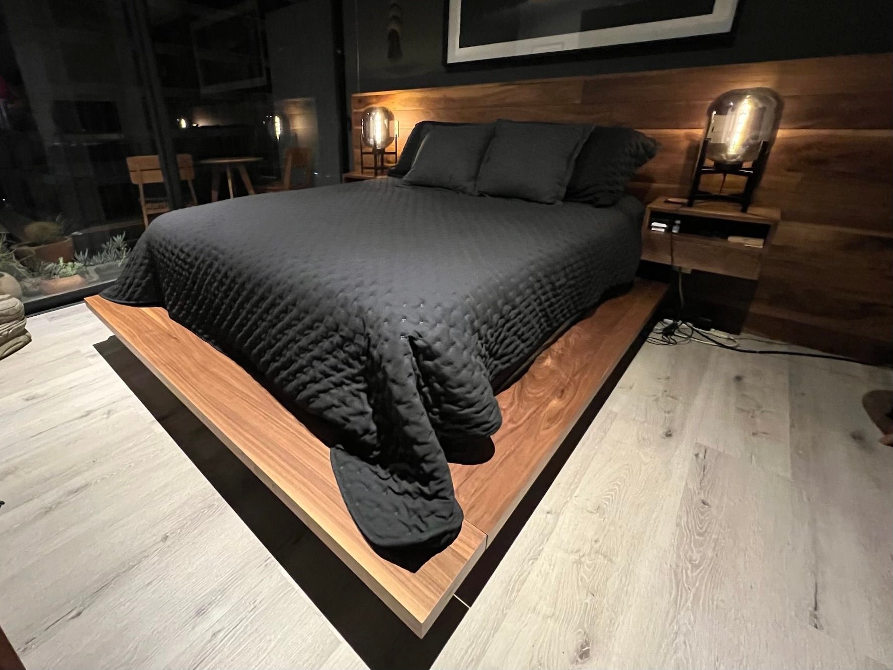 Bedroom with a Queen size Solid Walnut bedframe and a custom wall to wall solid Walnut headboard with floating sidetables. Bed has dark bedding and there are modern lamps on the sidetables